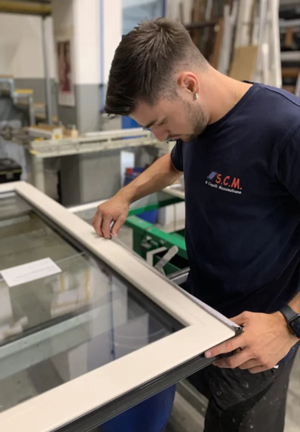 Artigiano con maglia S.C.M. di Capelli Massimiliano controlla un serramento in vetro con telaio bianco in laboratorio
